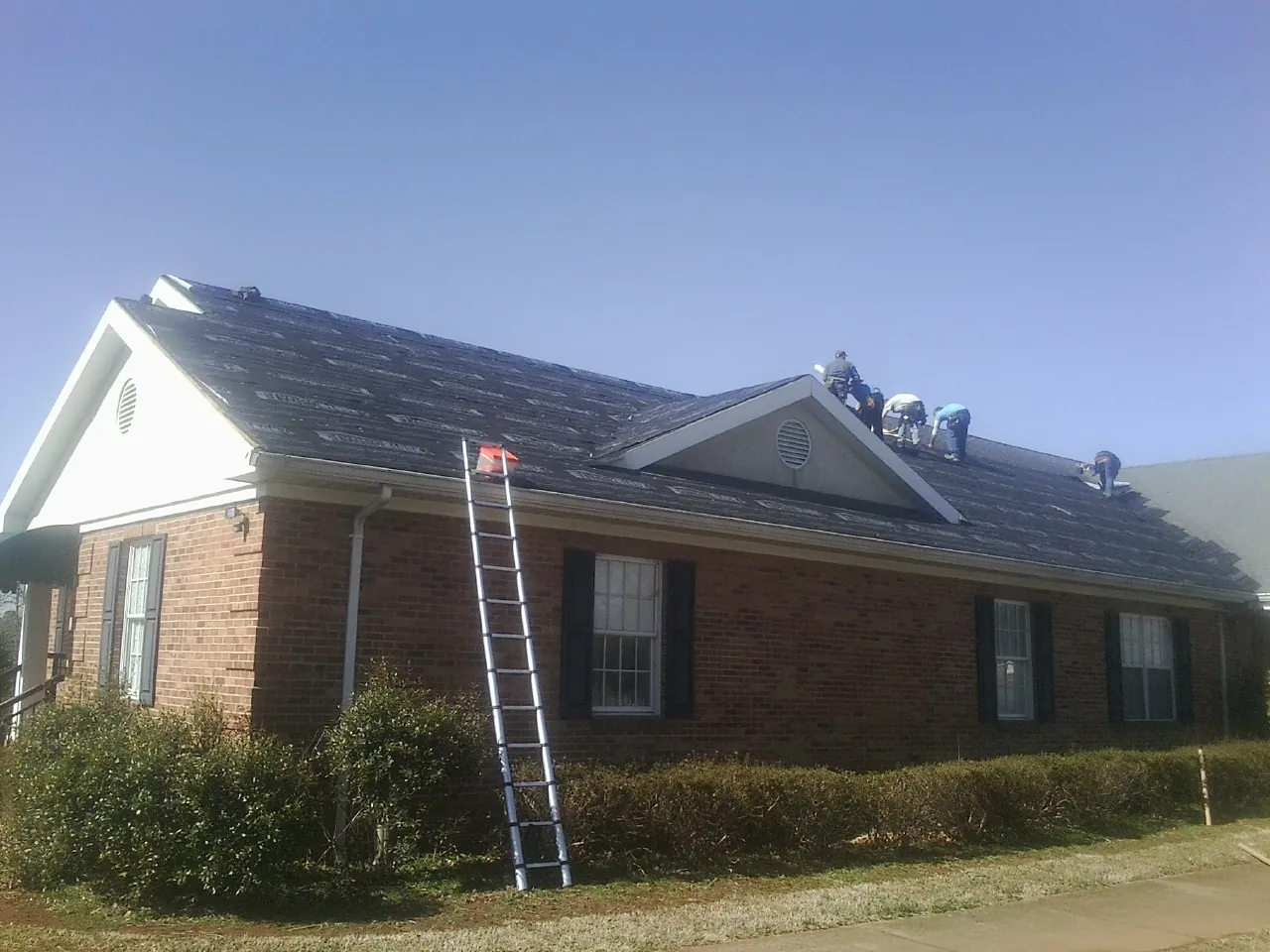 Crew tearing shingles off a brick ranch roof with a ladder set — Metal Roof Repair work by our crew in Clinton