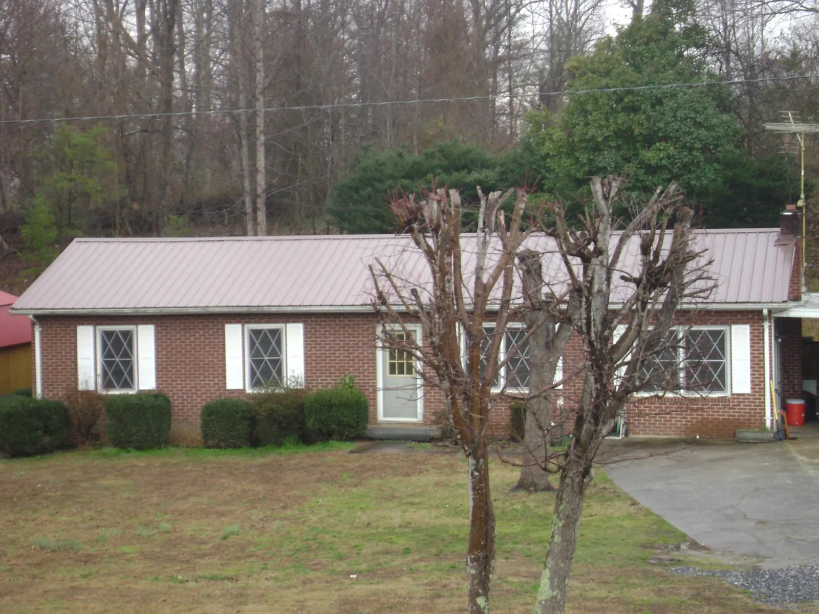 Mauve metal roof on a brick ranch home behind bare trees in Clinton